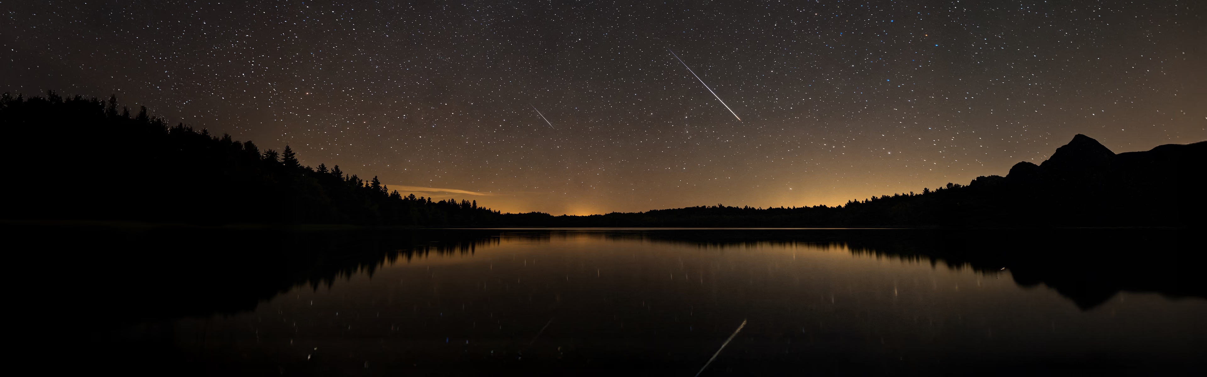 Sternenhimmel mit mehreren Sternschnuppen über einem Bergsee in ruhiger nächtlicher Atmosphäre, die zu Besinnung und innerer Reflexion einlädt.