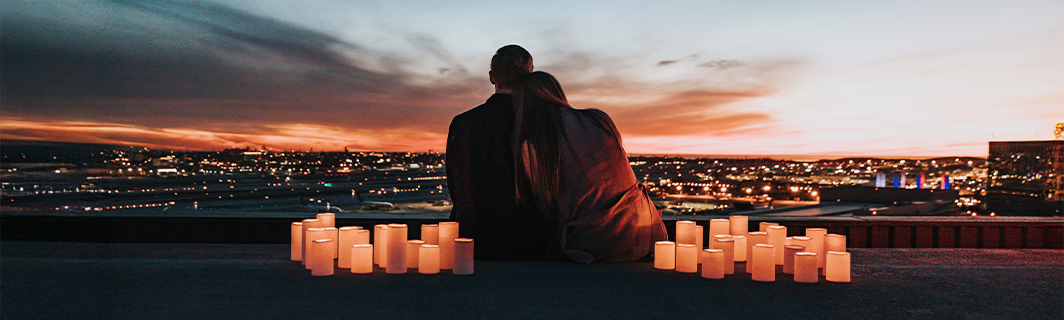 Ein Paar, das sich vor einer bei Sonnenuntergang beleuchteten Stadt umarmt, umgeben von Kerzen – ein Symbol für tiefe Liebe, innige Verbundenheit und Harmonie in der Beziehung