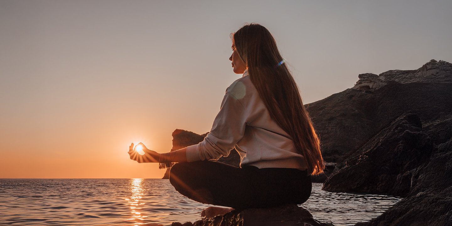 Frau meditiert bei Sonnenuntergang am Meer und symbolisiert innere Ruhe, geistige Klarheit und spirituelles Wachstum durch Meditation.